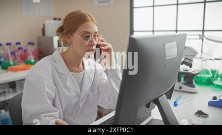 Focused caucasian woman scientist using computer and phone in a laboratory setting. Stock Photo