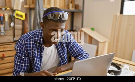 Smiling african man using laptop in a woodworking workshop. Stock Photo