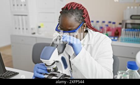 African american woman scientist with braids using microscope in laboratory Stock Photo