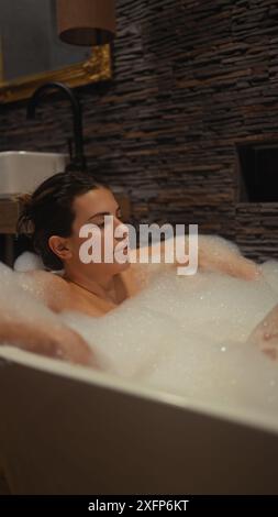A serene woman relaxes in a luxurious bath, evoking tranquility in a modern bathroom setting. Stock Photo