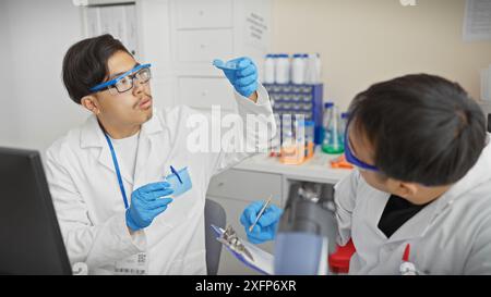 Two male scientists working together in a laboratory, examining samples, wearing lab coats and protective gloves. Stock Photo