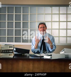 Overwhelmed office worker buried in paperwork at cluttered desk, surrounded by urgent notes and deadlines, illustrating stress, workload pressure Stock Photo