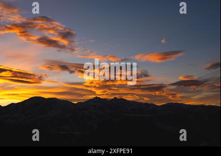 Dark orange landscape, mountains silhouette with a view of sunset sunbeams glowing behind the clouds Stock Photo