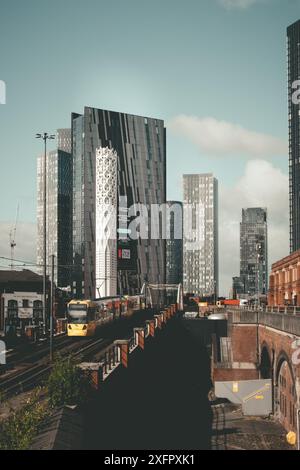 A Bee Network tram on the Metrolink Network in Manchester.  In the background the skyscrapers of Deansgate Square, and the Tower of Light. Stock Photo