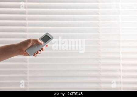 Man using remote control to adjust window blinds indoors, closeup. Space for text Stock Photo