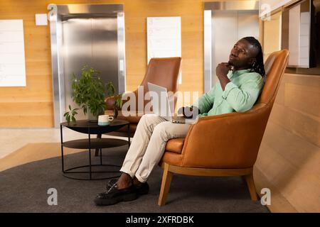 Working on laptop, man sitting in modern office lounge, thinking deeply Stock Photo