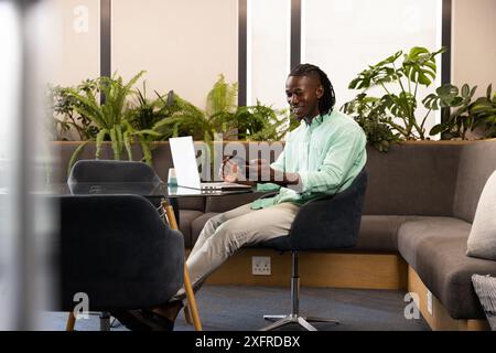 Using smartphone and laptop, man working in modern office with plants Stock Photo