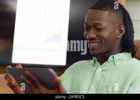 Using tablet, man smiling while analyzing financial data on screen in office Stock Photo
