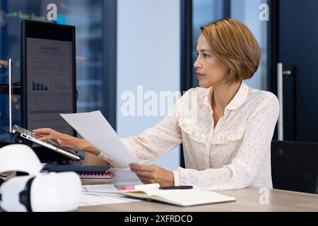 Working in office, woman analyzing financial report on computer and holding document Stock Photo