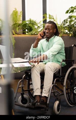 Using laptop and talking on phone, man in wheelchair working in office Stock Photo