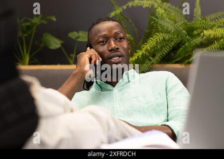 Talking on smartphone, man working on laptop in modern office setting Stock Photo