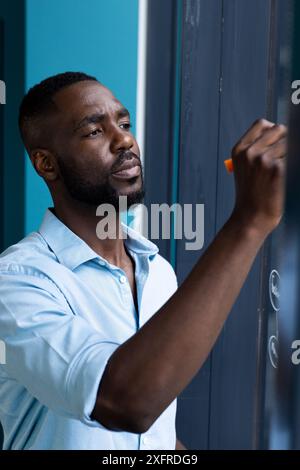 Writing on glass board, man in blue shirt focusing on work in office Stock Photo
