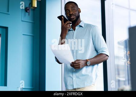 Holding document, man speaking on smartphone in modern office setting Stock Photo