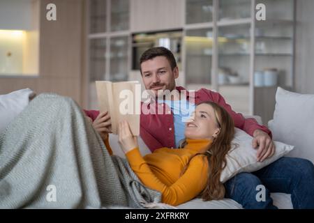Happy couple relaxing on couch, reading book. Spouses spend quality peaceful time together, resting. Stock Photo