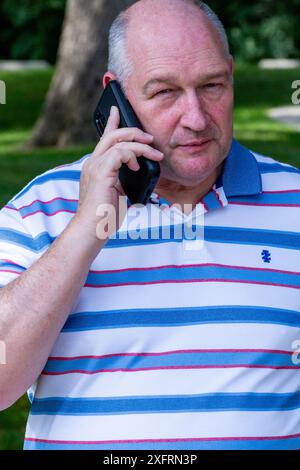 A balding middle aged man in a striped shirt using a cell phone. Stock Photo