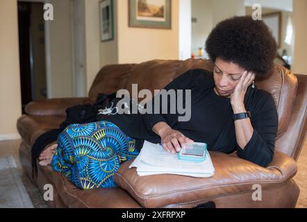 Smiling middle-aged African American woman studying at a table in dining room. Stock Photo