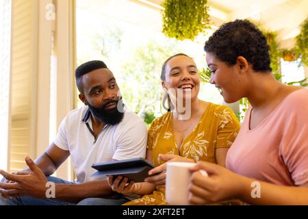 Smiling diverse friends sitting together, using tablet and drinking coffee at home Stock Photo