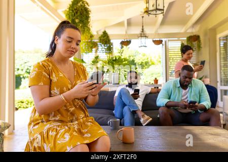 Using smartphones, group of diverse friends relaxing together on patio Stock Photo