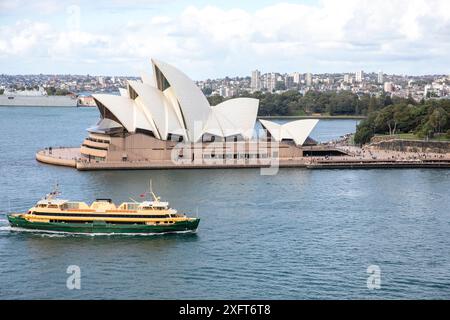 Sydney Opera House with MV Freshwater ferry passing by, Garden Island naval base with HMAS Canberra in port, Sydney,NSW,Australia Stock Photo