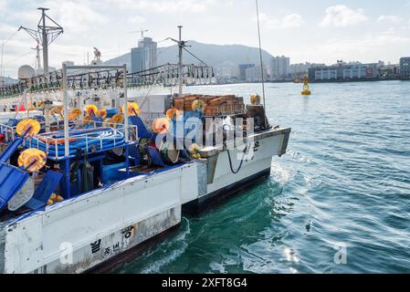 Busan, South Korea - October 7, 2017: Two fishing vessels parked at Busan Harbor. The city is visible on blue sky background. Stock Photo