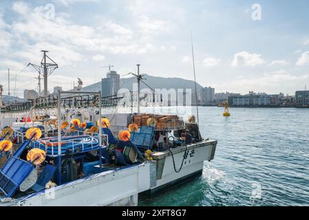 Busan, South Korea - October 7, 2017: Two fishing vessels parked at Busan Harbor. The city is visible on blue sky background. Stock Photo