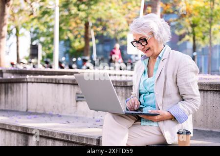 mature woman smiling happy using laptop at city Stock Photo