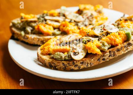 Plate with two slices of avocado toasts with mushrooms and vegan cheddar (carrots, nutritional yeast, mustard) Stock Photo