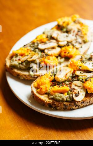 Plate with two slices of avocado toasts with mushrooms and vegan cheddar (carrots, nutritional yeast, mustard) Stock Photo