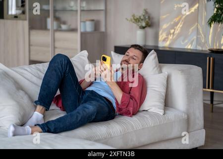 Relaxed guy resting using mobile phone, watching videos, posts, news online on internet social media Stock Photo
