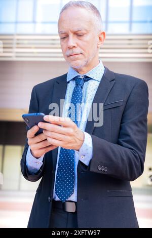 Businessman using an app on his smartphone and standing outdoors.Vertical Stock Photo