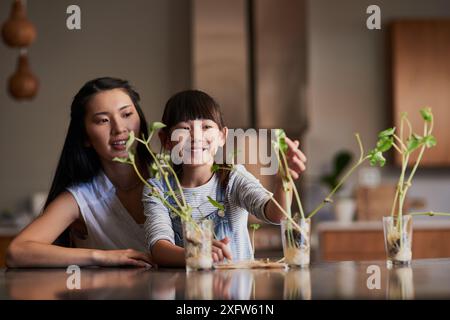Plants, growth and kid with mom in home for sustainable indoor gardening for science project. Research, botany and Asian mother helping girl child Stock Photo