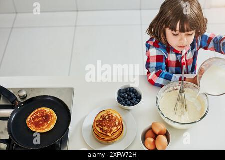 Boy, baking and top with bowl in kitchen, ingredients and mixing or pancake batter in morning apartment. Culinary skills, kid and mixture or cooking Stock Photo