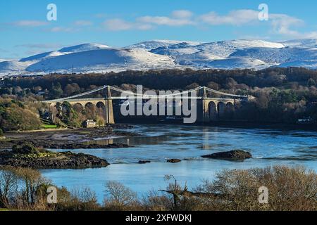 Menai Suspension Bridge, designed by Thomas Telford, viewed from Anglesey across Menai Strait, with snow capped hills in background. North Wales, UK. December 2017 Stock Photo