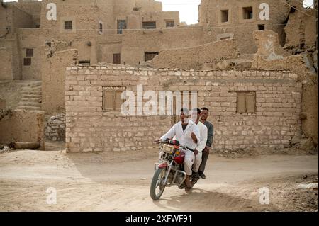 Three Egyptian men riding a motorcycle in the ruins of Shali fortress. The Siwa Oasis, an urban oasis in Egypt situated between the Qattara Depression and the Great Sand Sea in the Western Desert of North Africa. Stock Photo