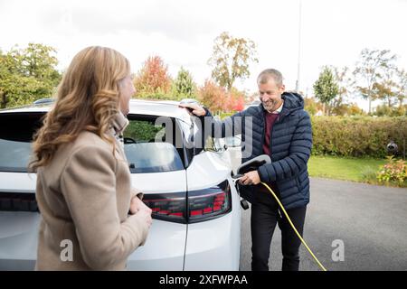 Smiling mature man standing by woman charging electric car Stock Photo