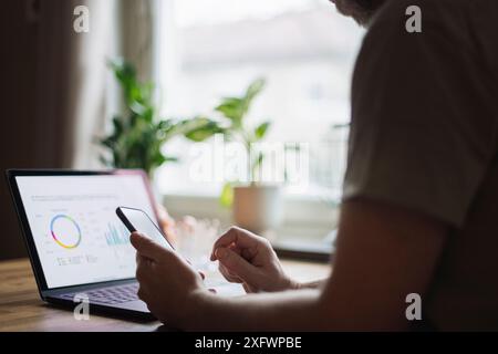 Male freelancer using smart phone near laptop at home office Stock Photo