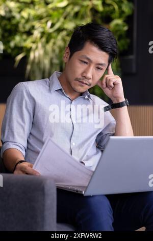 Working from office, man reviewing documents while using laptop on couch Stock Photo