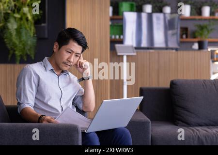 Working from office, man using laptop and reviewing documents on couch, copy space Stock Photo