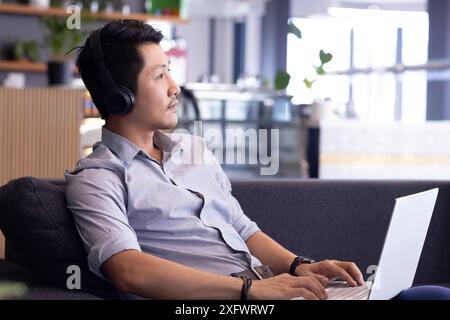 Using laptop and wearing headphones, man working remotely in modern office Stock Photo