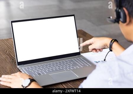 Pointing at blank laptop screen, man wearing headset working from business, copy space Stock Photo
