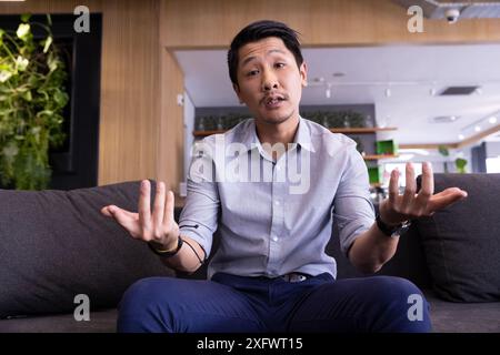 Man sitting on couch gesturing with hands, engaging in conversation indoors Stock Photo