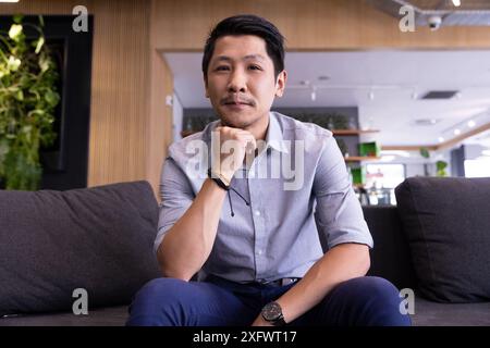 Sitting on couch, man in casual attire posing confidently in modern office Stock Photo