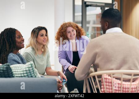 Cheerful female colleagues sharing ideas with businessman in office Stock Photo