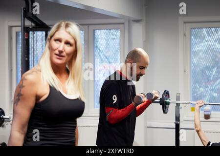 Bald man exercising with dumbbell while blond woman talking at gym Stock Photo
