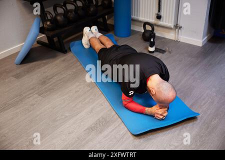 Bald man doing plank on exercise mat at gym Stock Photo