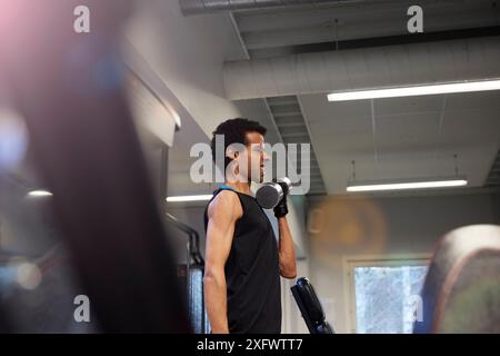 Young man exercising with dumbbell while making a face at gym Stock Photo