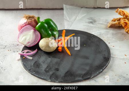 Empty black circular plate with vegetables on the side for food product placement. Stock Photo