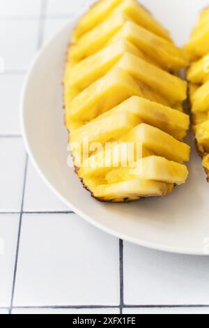 Two beautifully sliced pineapple halves on a white plate, placed on a tiled surface Stock Photo