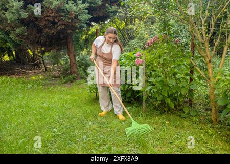 Raking leaves. Female is raking leaves with a rake. Picture of woman working with tools in the garden Stock Photo