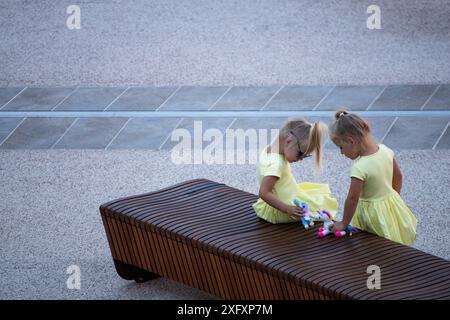 Twin sisters playing together on bench in park Stock Photo